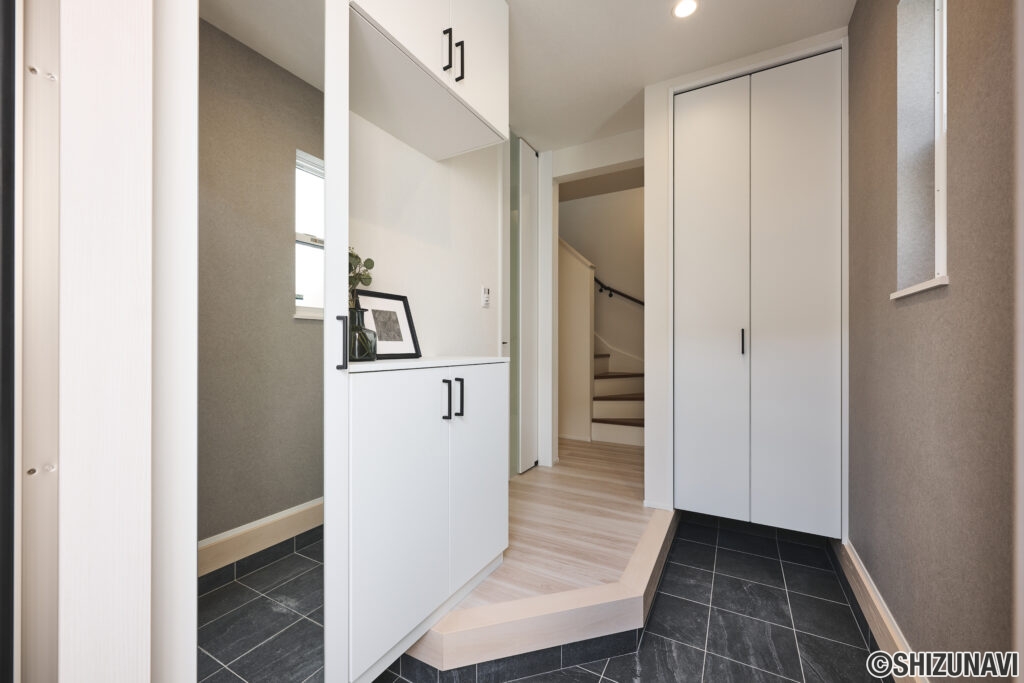 玄関ドアを開けると、明るく開放的な玄関ホールが迎えてくれます。白を基調としたシューズボックスと建具が空間を広く見せ、グレーのタイルと壁面が落ち着いた印象をプラス。