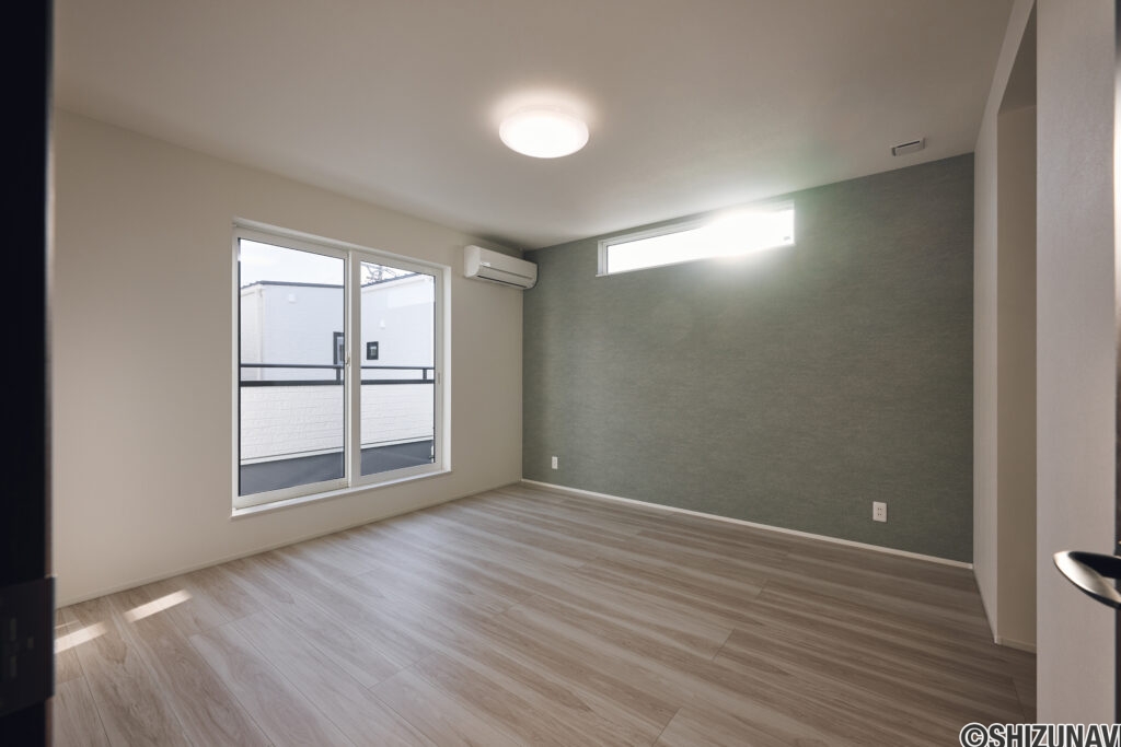 【B棟】 落ち着いた色合いのアクセントクロスが、空間に上質な雰囲気を添える洋室。大きな窓と高窓からやわらかな光が入り、寝室にも適した心地よい空間です。