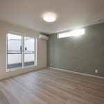 【B棟】 落ち着いた色合いのアクセントクロスが、空間に上質な雰囲気を添える洋室。大きな窓と高窓からやわらかな光が入り、寝室にも適した心地よい空間です。