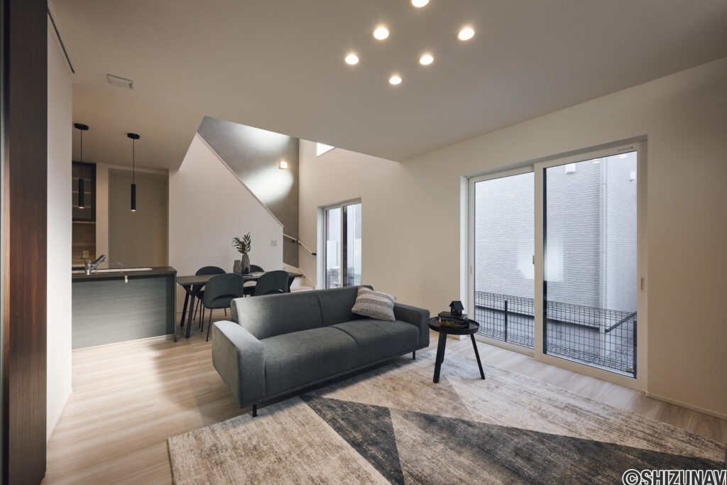 【B棟】吹き抜けから自然光がたっぷり差し込む、明るく開放的なLDK。家事動線にも配慮した間取りと、モノトーンでまとめたシンプルモダンな空間です。