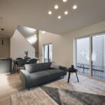 【B棟】吹き抜けから自然光がたっぷり差し込む、明るく開放的なLDK。家事動線にも配慮した間取りと、モノトーンでまとめたシンプルモダンな空間です。