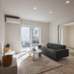 【A棟】大きな窓から差し込む自然光が、リビング全体を明るく包み込む開放的な空間。落ち着いたトーンのインテリアが心地よさを演出し、隣接する和室と一体で使えるゆとりある住まいです。