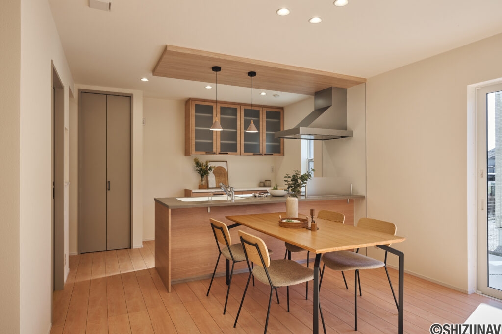 【B棟】木目のキッチンと天井が、空間にほっとする温もりをプラス。やわらかな質感に包まれて、家族の会話も自然と弾む、安心感のあるダイニングです。
