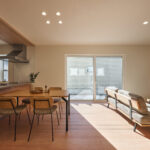 【B棟】大きな窓から光がたっぷり差し込む、のびやかなLDK。木目のキッチンと家具がやさしく調和し、食事もくつろぎも家族の時間が自然と深まる空間です。