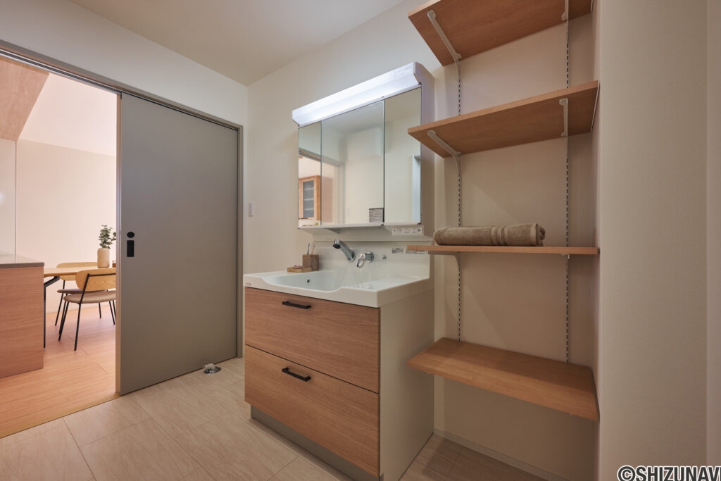 【B棟】木目の洗面台がやさしく映える洗面室。可動棚付きでタオルや洗剤、家族のストックをすっきり収納でき、朝の身支度も夜の片付けもスムーズに整います。