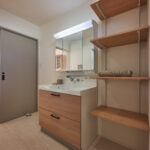 【B棟】木目の洗面台がやさしく映える洗面室。可動棚付きでタオルや洗剤、家族のストックをすっきり収納でき、朝の身支度も夜の片付けもスムーズに整います。