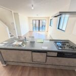 １号棟　キッチン３口のガスコンロ・グリル・食洗器付きのキッチン。目線がすっきりしてますので、開放感◎調味料の小物なども収納できるスペースあり。収納力も高いです。コンロの横の壁は、掃除しやすい素材という気遣いもうれしいですね。